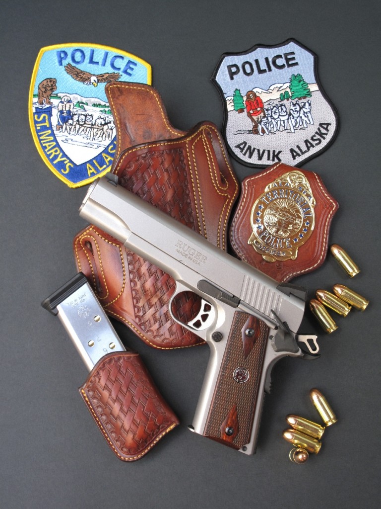 Le pistolet Ruger modèle SR1911, accompagné d’écussons brodés (patches) de la police en Alaska et d’un ensemble en cuir« basket », composé d’un holster, d’un porte-chargeur et d’un porte insigne (badge), réalisé par la maison française La sellerie du Thymerais.